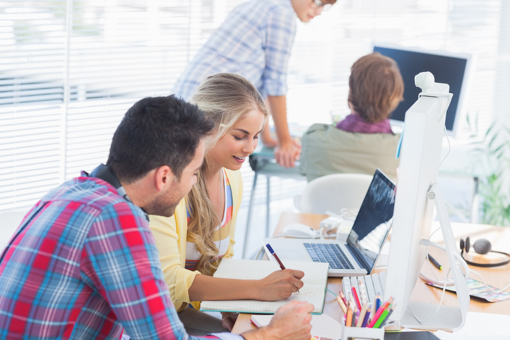 Cheerful designers working on a document with colleagues discussing behind